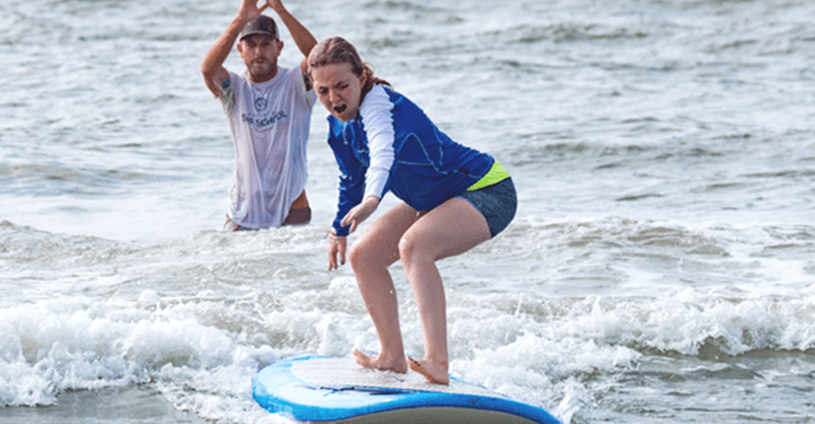 girl surfing on water with person in the background