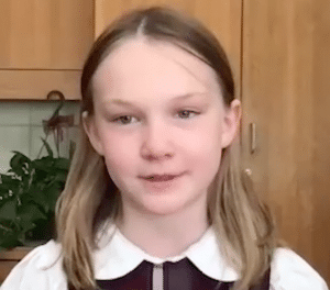 Picture of young girl with shoulder length blonde hair, a collared white and brown shirt and gray eyes, smiling