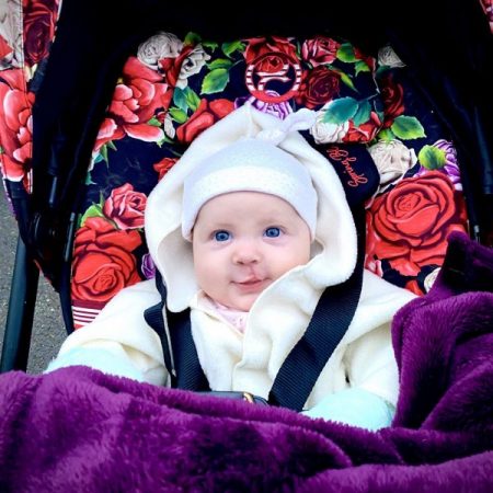 myFace - Harlyn Rae Picture Picture of baby in a baby carrier decorated with rose background. The baby girl is wearing a white hat and coat, has blue eyes and is smiling. Also has a purple blanket