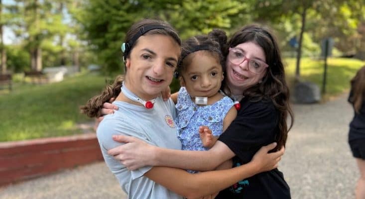 2 girls embracing a young child, all smiling